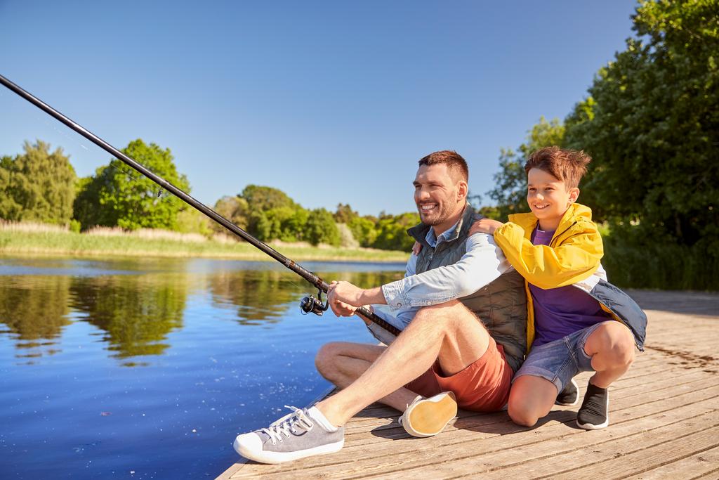 happy smiling father and son fishing on river Vater mit Sohn sitzen auf Bootssteg am See und angeln.