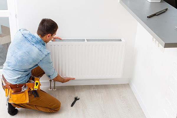 Heizungstausch (©iStock/Sinenkiy) Mann montiert einen Heizkörper an der Wand