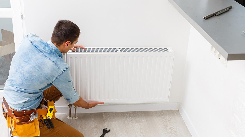 Heizungstausch (©iStock/Sinenkiy) Mann montiert einen Heizkörper an der Wand